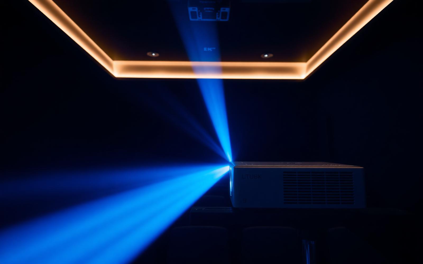 Digital cinema projector casting a blue beam of light in a dark projection booth