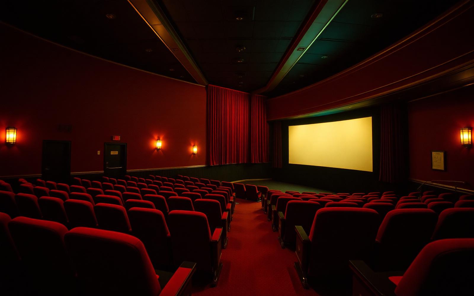 Empty red seats facing a glowing screen inside a classic small-town movie theatre auditorium